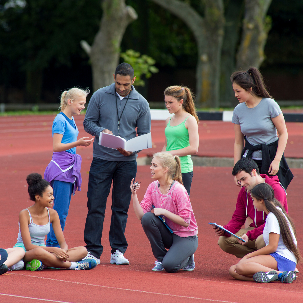 gym teacher gathered outside with students on a track
